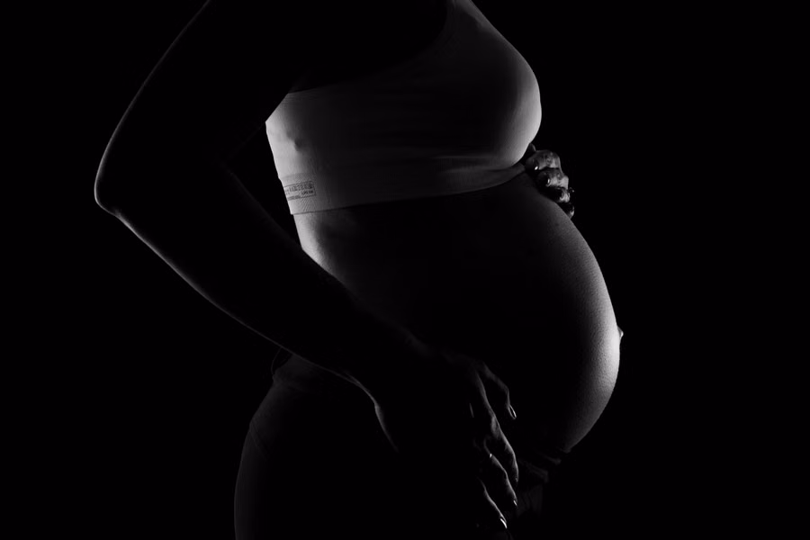 Close-up em preto e branco de mulher grávida segurando a barriga